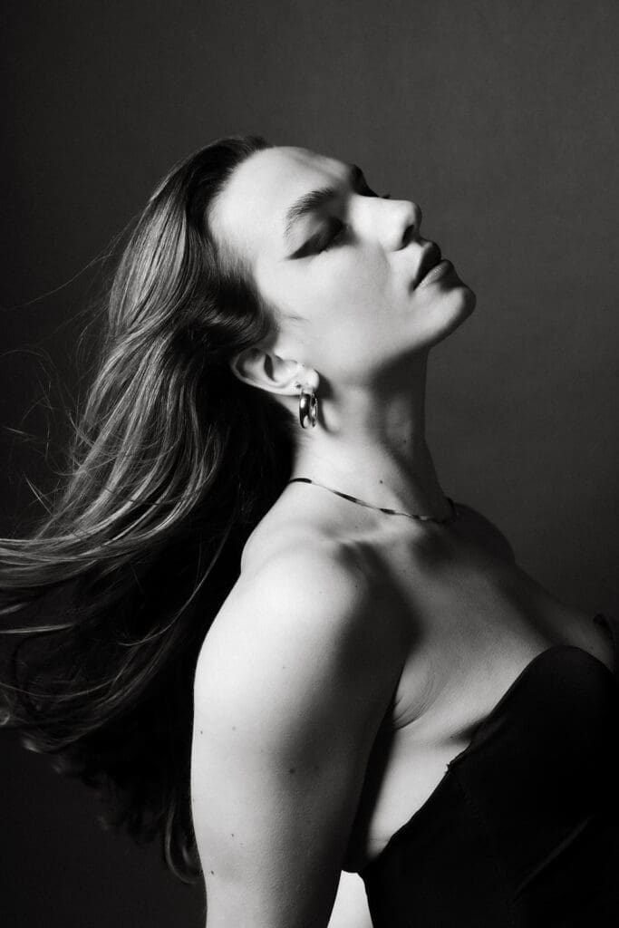 Dramatic and bold black and white portrait of a woman in front of a black backdrop.