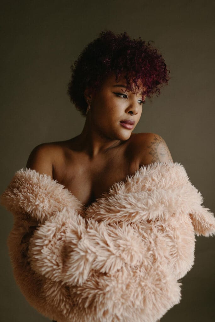 Portrait of a woman wrapped in a teddy coat in front of an olive green backdrop.