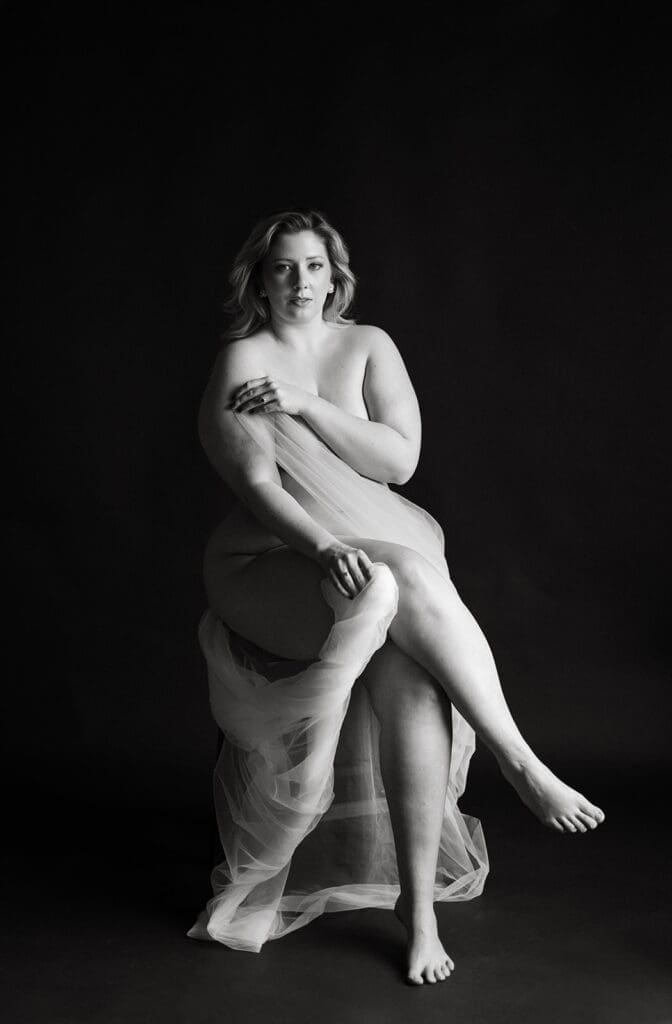 Fine Art black and white portrait of a woman in front of a backdrop.