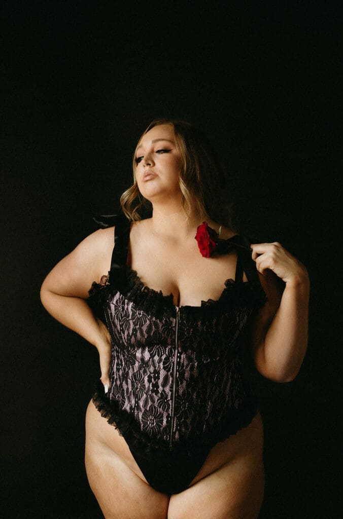 Portrait of a woman in a corset holding a rose in front of a Backdrop.