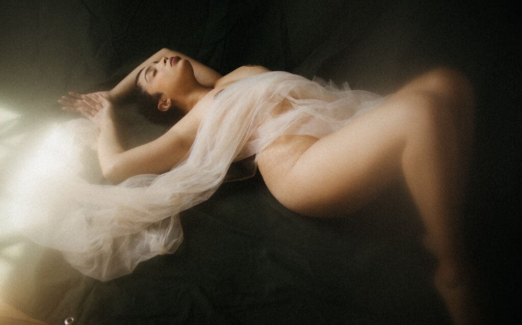Ethereal boudoir image of a woman wrapped in tulle on a Fine Art Backdrop