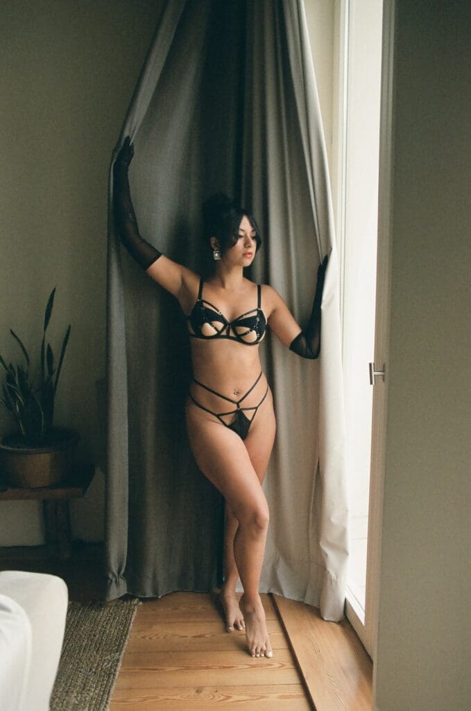 Boudoir photo shot on film in Porto, Portugal at the stunning Hotel Village by BOA. Woman standing in front of a window with natural light wearing lingerie and black gloves. 